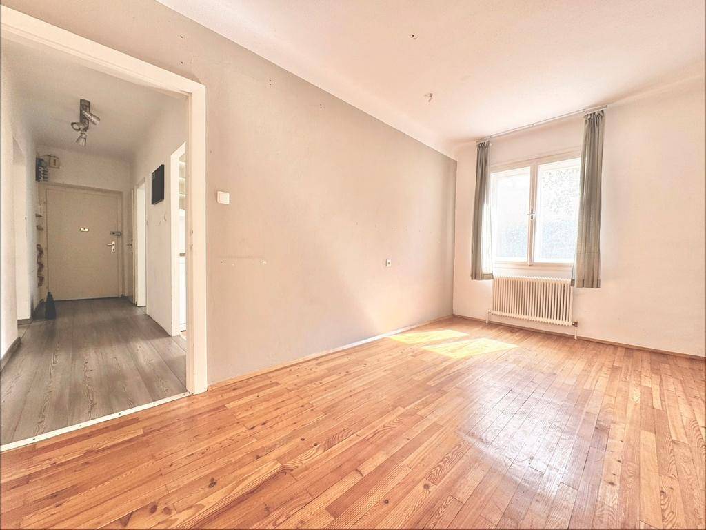 Heller Raum mit Holzboden, einer grauen Akzentwand und einem Fenster mit Vorhängen.