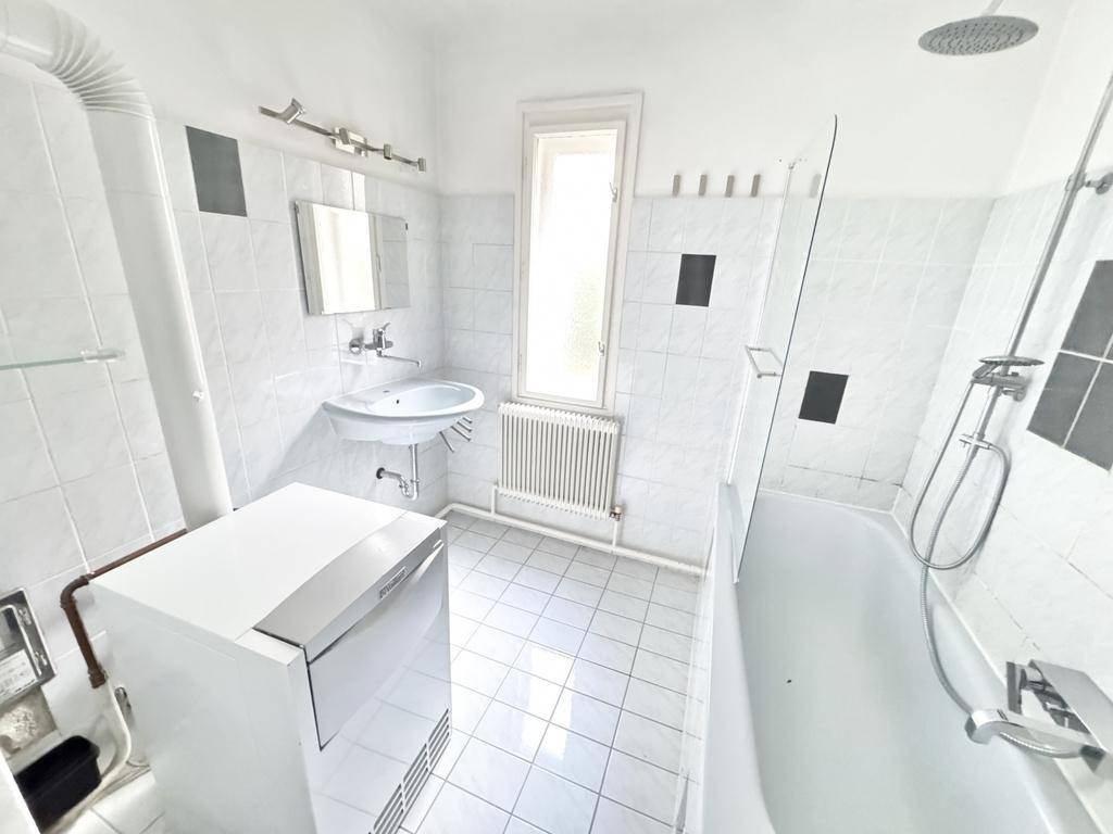 Gefliestes Badezimmer mit Badewanne, Dusche, Waschbecken, Fenster und Waschmaschine.
