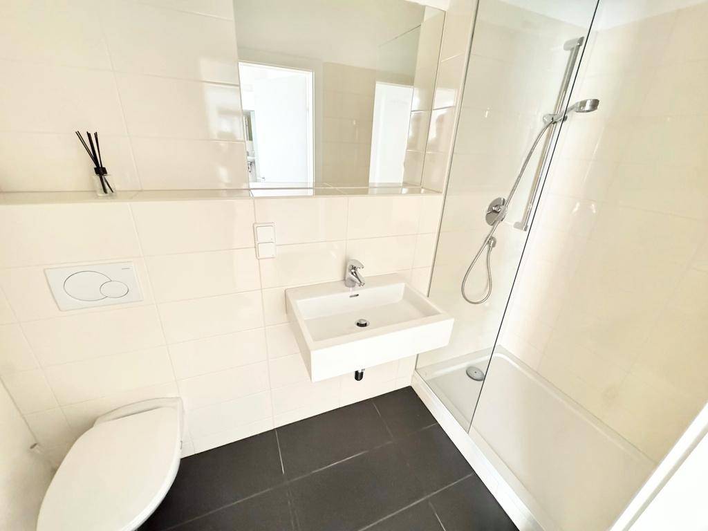 Helles Badezimmer mit moderner Dusche, Wand-WC und Waschbecken, alles in hellen Fliesen gehalten.