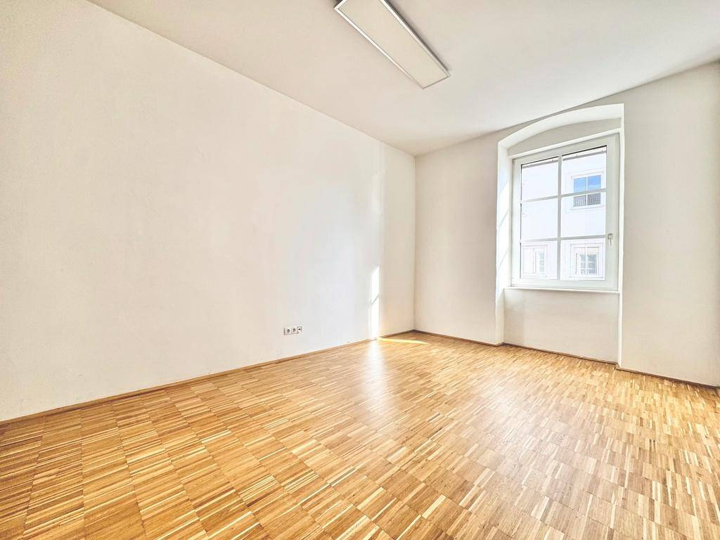 Helles Schlafzimmer mit klassischem Parkettboden, weißen Wänden und einem großen Fenster.