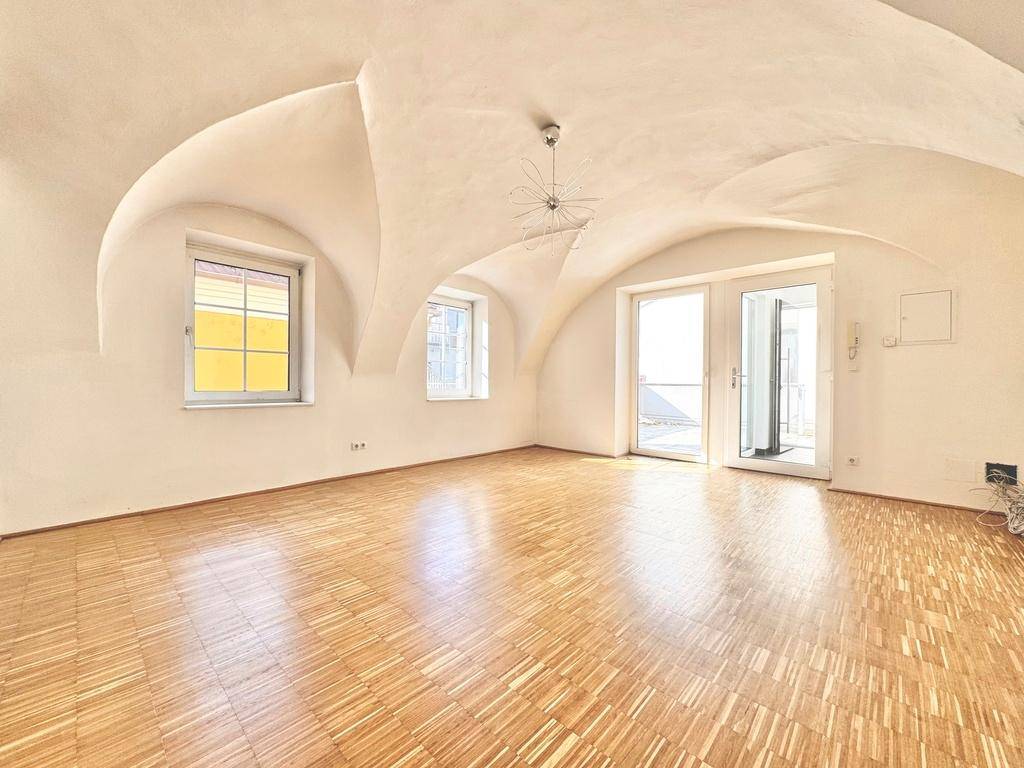 Heller Wohnraum mit beeindruckendem Gewölbedecke, Parkettboden und Zugang zu einer Terrasse.