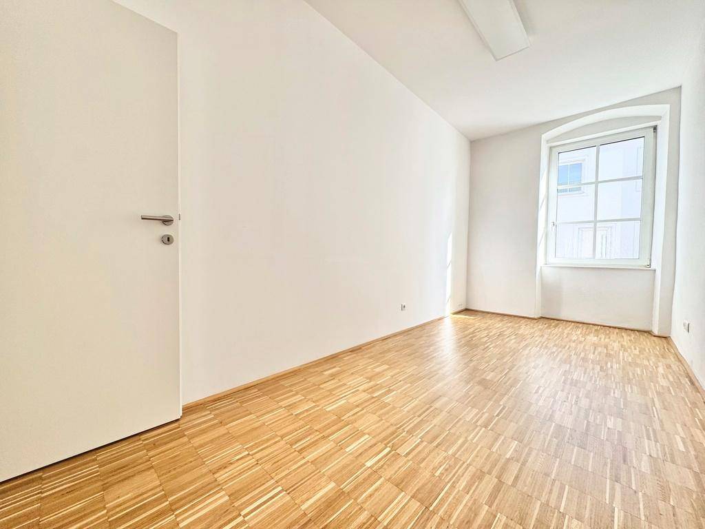 Leeres Zimmer mit Holzboden und weißer Tür, bereit für individuelle Gestaltung und Einrichtung.