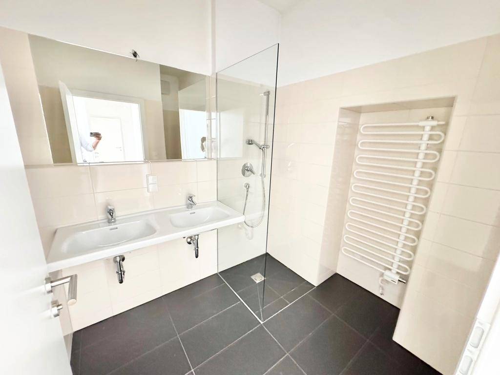 Modernes Badezimmer mit Doppelwaschbecken, ebenerdiger Dusche und Handtuchheizkörper.