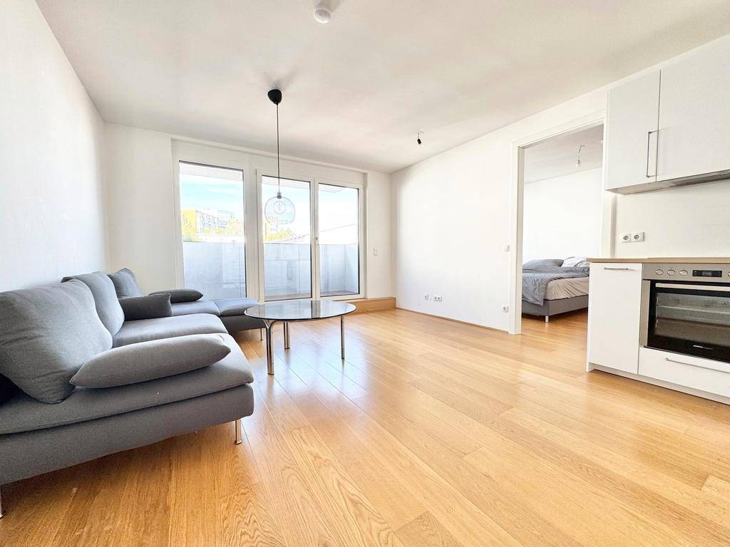 Heller Wohnbereich mit Holzboden, gemütlichem Sofa und offener Verbindung zum Schlafzimmer und einer Küchenzeile.