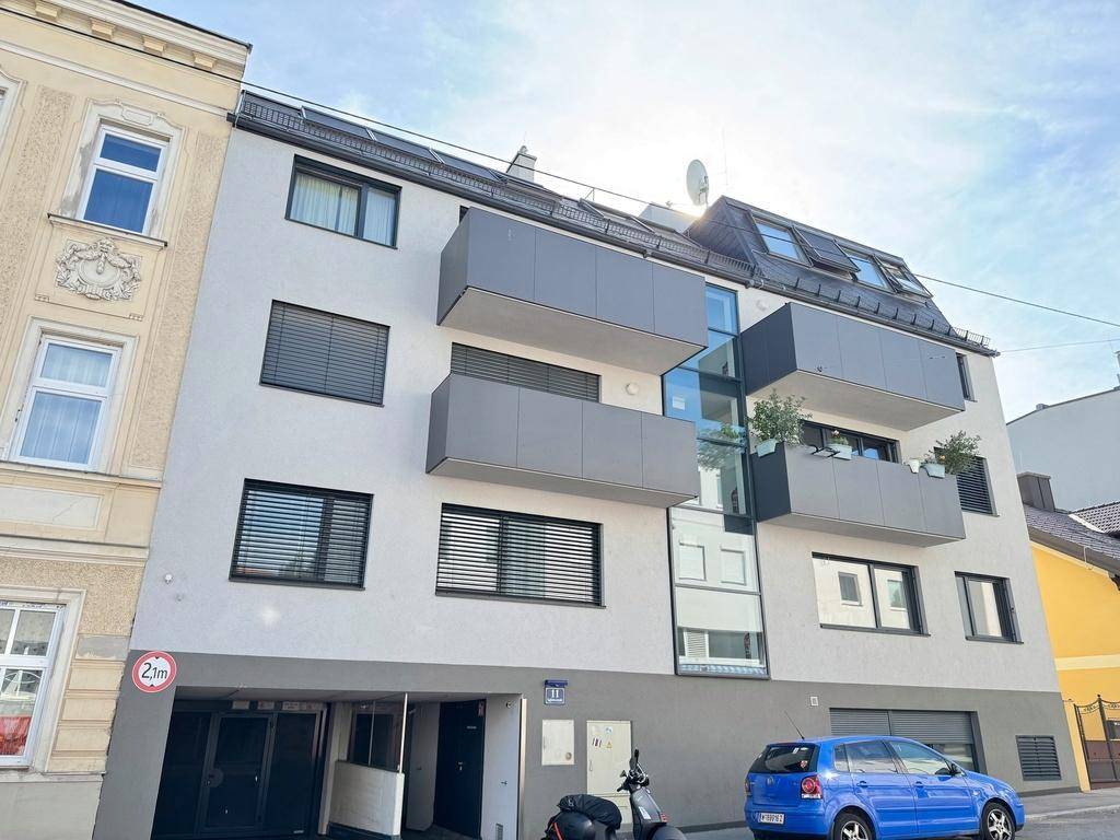 Moderne Wohnhausfassade mit grauen Balkonen, großen Fenstern und dunklen Jalousien.