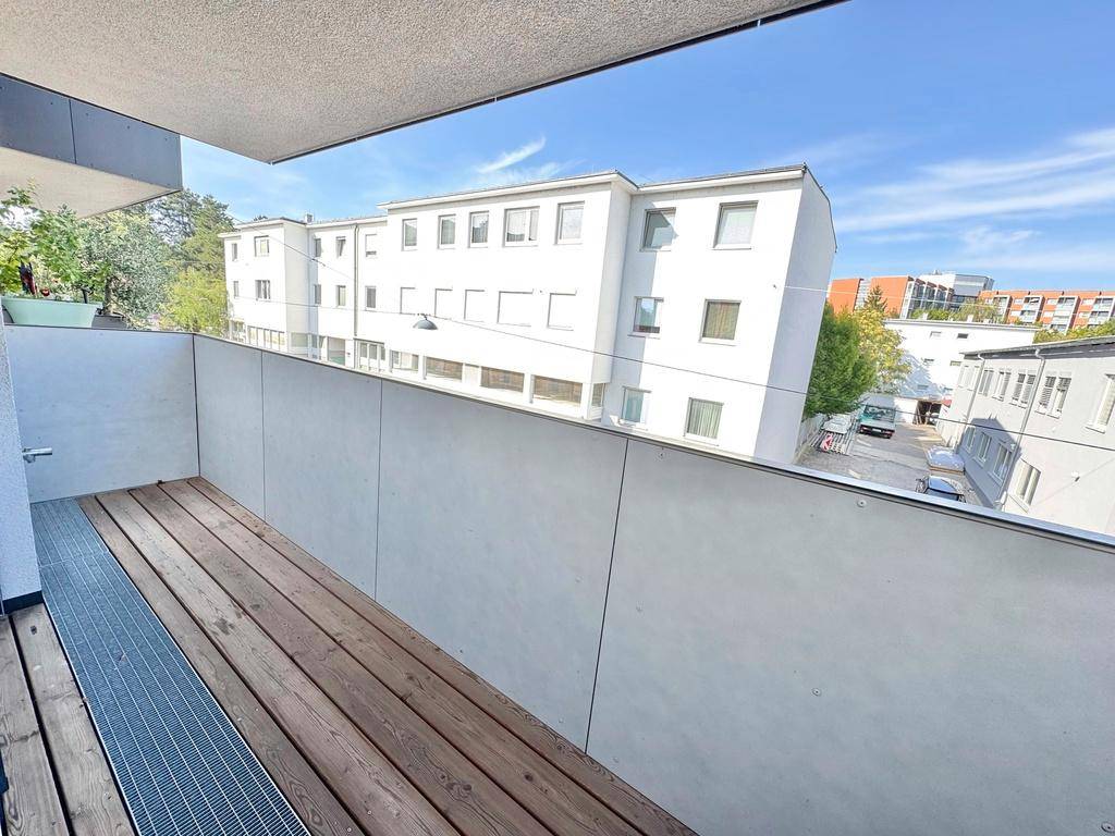 Schlichter Balkon mit Holzboden und einer weiten Aussicht auf umliegende Wohngebäude.