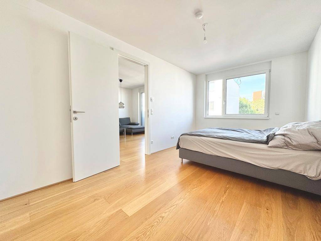 Helles Schlafzimmer mit Holzboden und direktem Zugang zum Wohnbereich durch eine Schiebetür.