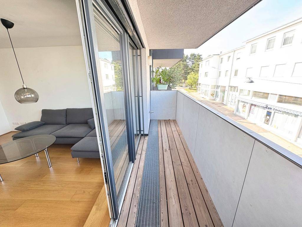 Geräumiger Balkon mit Holzdielen und Blick auf die Straße, direkt vom Wohnbereich zugänglich.