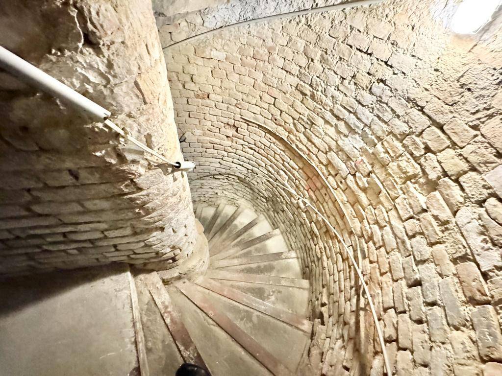 Historische Wendeltreppe aus Beton, umgeben von unverputzten Ziegelwänden im Kellerbereich.