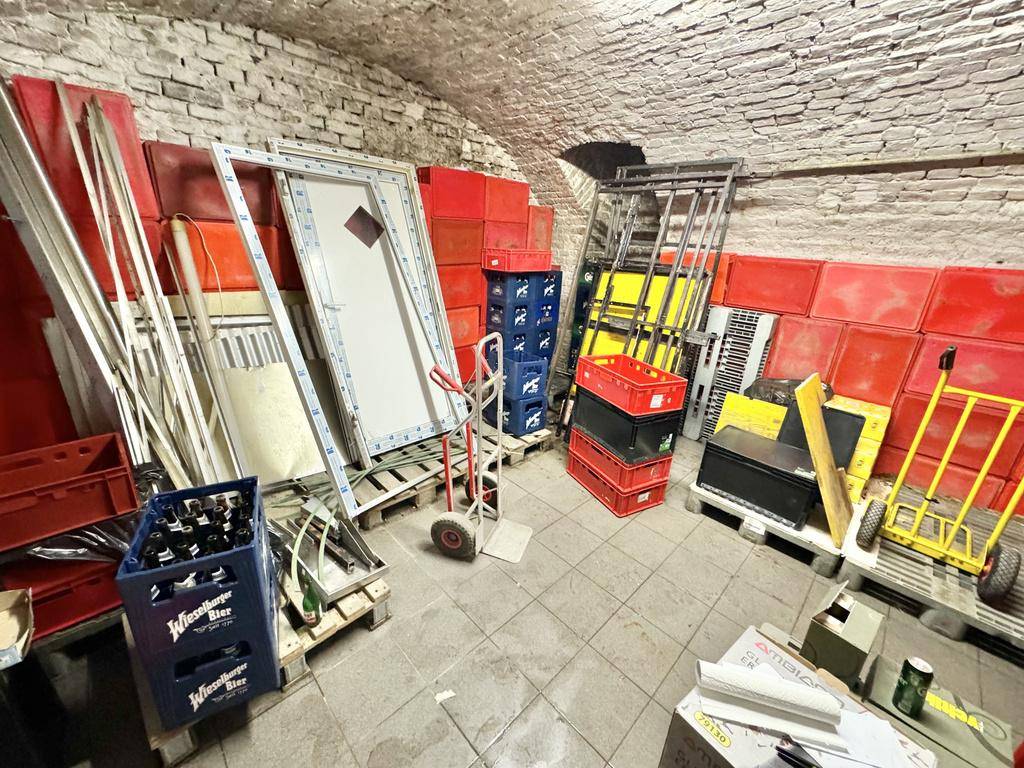 Historischer Kellerraum mit Ziegelgewölbe, gefliestem Boden und verschiedenen Materialien zur Lagerung.