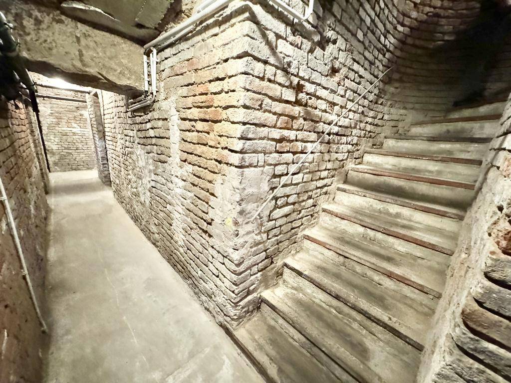 Kellerflur mit freiliegenden Ziegelwänden, Betonboden und einer Treppe nach oben führend.