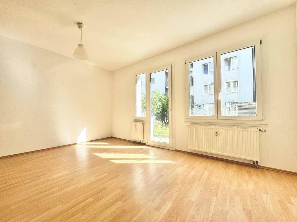 Geräumiger Wohnbereich mit hellem Laminatboden und großen Fenstern, die viel Tageslicht hereinlassen.