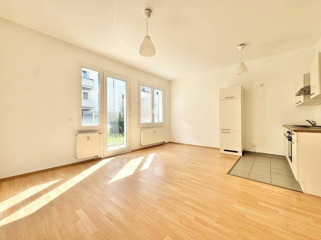 Lichtdurchfluteter Wohnraum mit Laminatboden, Zugang zum Garten und einer kleinen Küchenzeile.