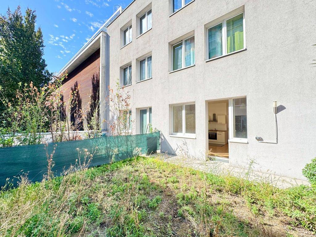 Erdgeschosswohnung mit direktem Zugang zu einem ungepflegten Gartenbereich und Blick auf die Fassade.