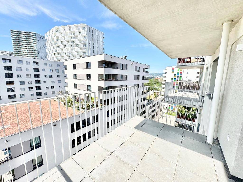 Blick vom Balkon auf moderne Wohngebäude in einer städtischen Umgebung unter blauem Himmel.