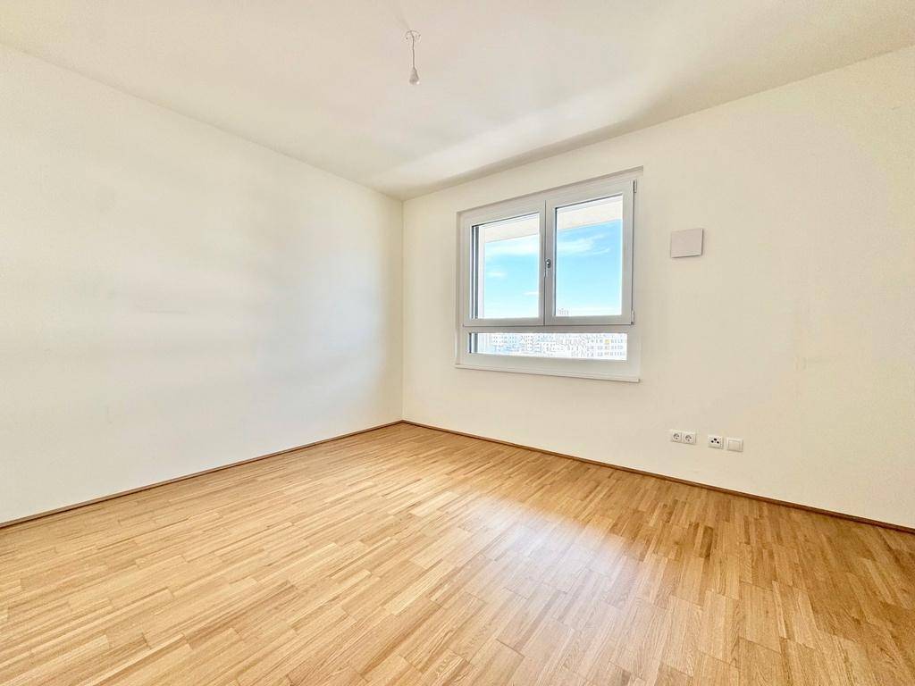 Helles Schlafzimmer mit Parkettboden und großem Fenster für viel Tageslicht und Ausblick.