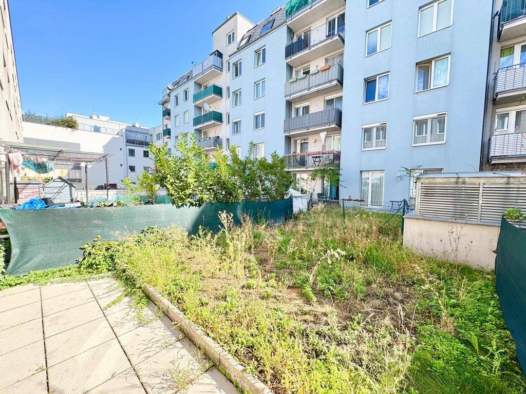 Blick auf die Rückseite eines Wohnhauses mit mehreren Balkonen und einem verwilderten Gartenbereich.