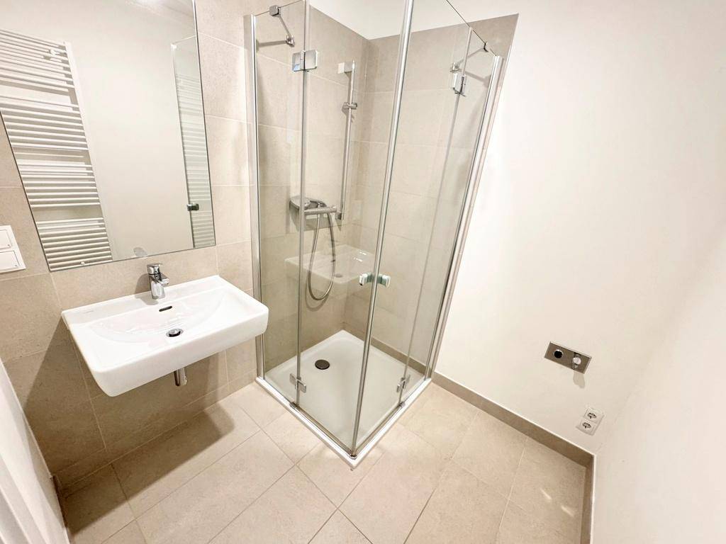 Modernes Badezimmer mit Eckdusche, Einzelwaschbecken und beheiztem Handtuchhalter in neutralen Farben.