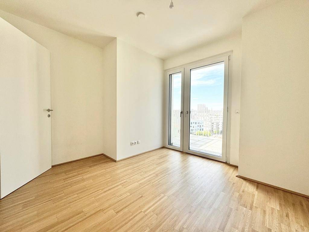 Schlafzimmer mit direktem Zugang zum Balkon und hellem Parkettboden, ideal für frische Luft.