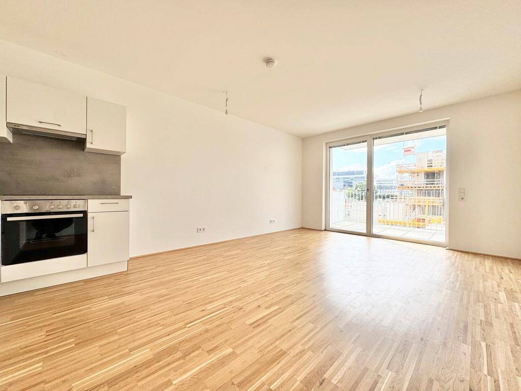 Offener Wohnbereich mit Parkettboden, integrierter Küchenzeile und Zugang zu einem sonnigen Balkon.