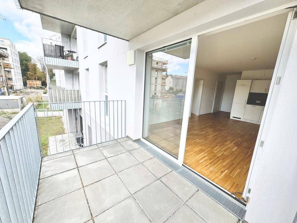 Geräumiger Balkon mit Fliesen und Zugang zu einem hellen Wohnbereich mit Holzboden und Küche.