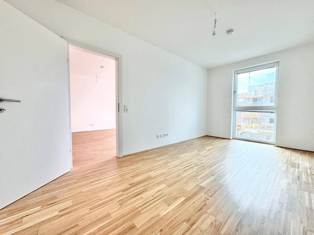 Helles Schlafzimmer mit Parkettboden, weißen Wänden und Fenster mit Blick auf die Baustelle.