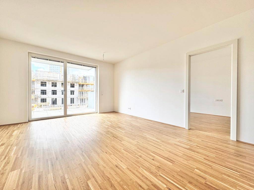 Helles Wohnzimmer mit Parkettboden, weißen Wänden und großem Fenster mit Zugang zum Balkon.
