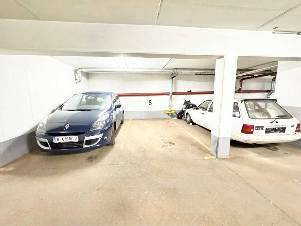 Zwei geparkte Fahrzeuge in einem Tiefgaragenstellplatz mit Betonboden und tragenden Säulen.