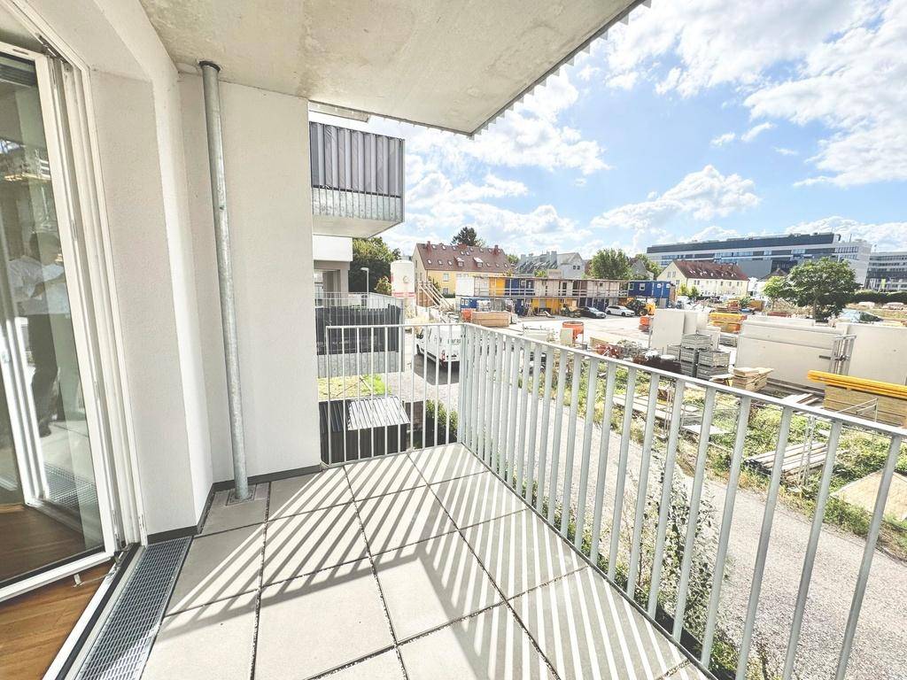 Sonniger Balkon mit Fliesenboden und weitem Blick über eine Baustelle und die städtische Umgebung.
