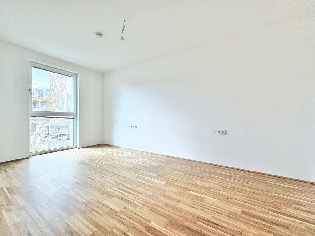 Geräumiges Schlafzimmer mit hellem Parkettboden und großem Fenster, das viel Tageslicht hereinlässt.