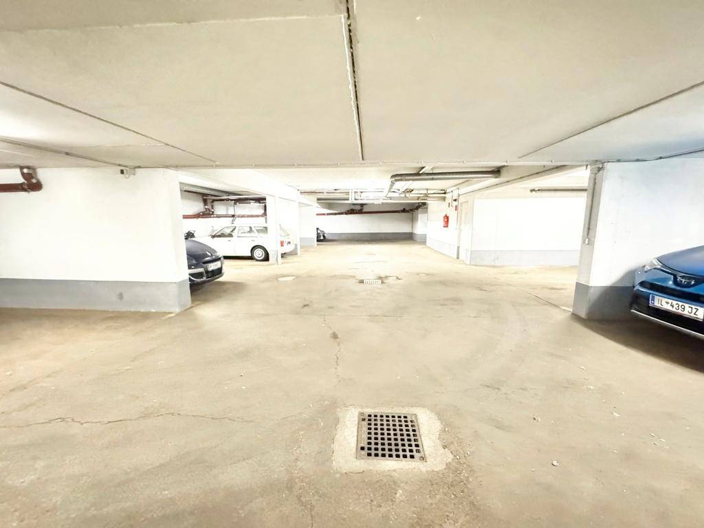 Geräumige Tiefgarage mit mehreren Stellplätzen, Betonboden und Entwässerungssystem, gut beleuchtet.