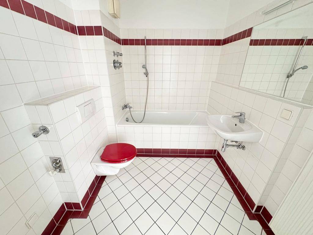 Badezimmer mit weißen Fliesen, rotem Akzent und Badewanne, ausgestattet mit WC und Waschbecken.