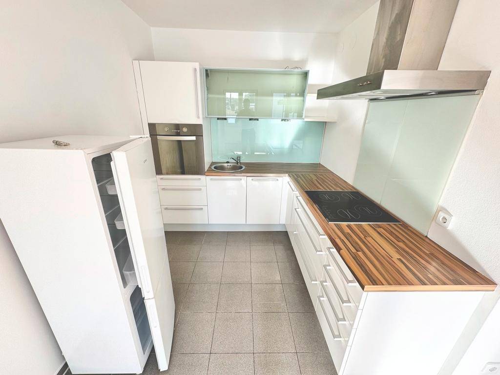 Funktionale Küche mit weißen Schränken, Holzarbeitsplatte und integrierten Geräten, inklusive Kühlschrank.