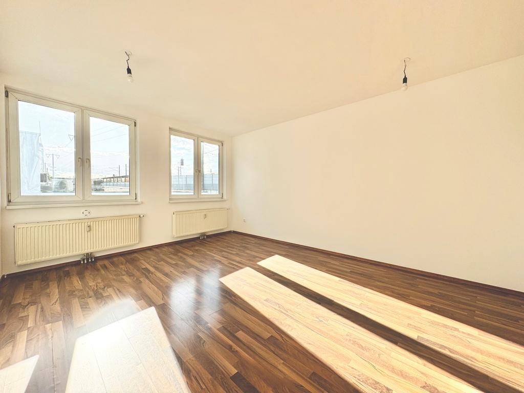 Geräumiges, leeres Zimmer mit Laminatboden und zwei großen Fenstern, die viel Tageslicht hereinlassen.