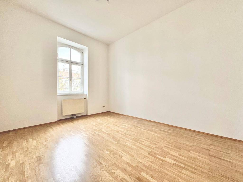 Helles Schlafzimmer mit klassischem Parkettboden und einem Fenster, bereit zur Einrichtung.