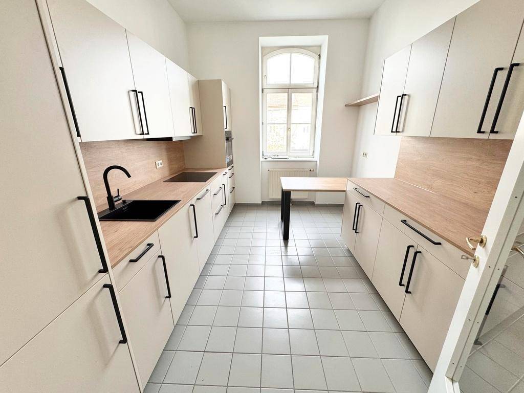 Moderne Küche mit hellen Schränken, Holzarbeitsplatten und integrierten Geräten, inklusive Fenster.