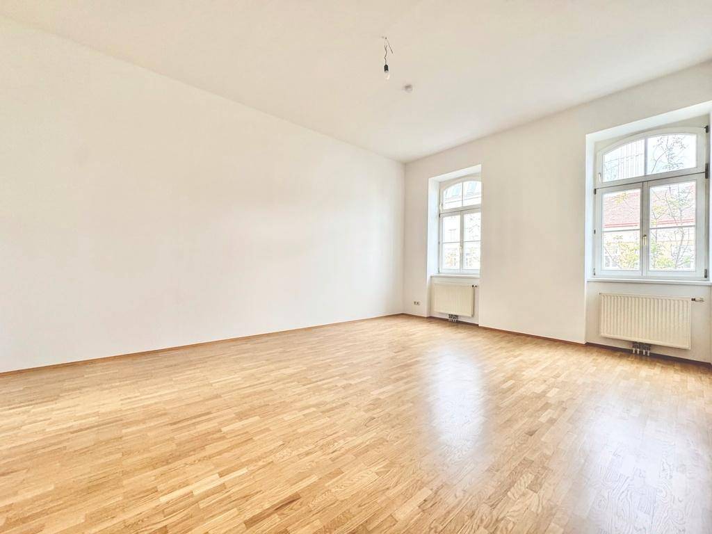Heller, leerer Raum mit warmem Parkettboden und zwei Fenstern, die eine angenehme Atmosphäre schaffen.