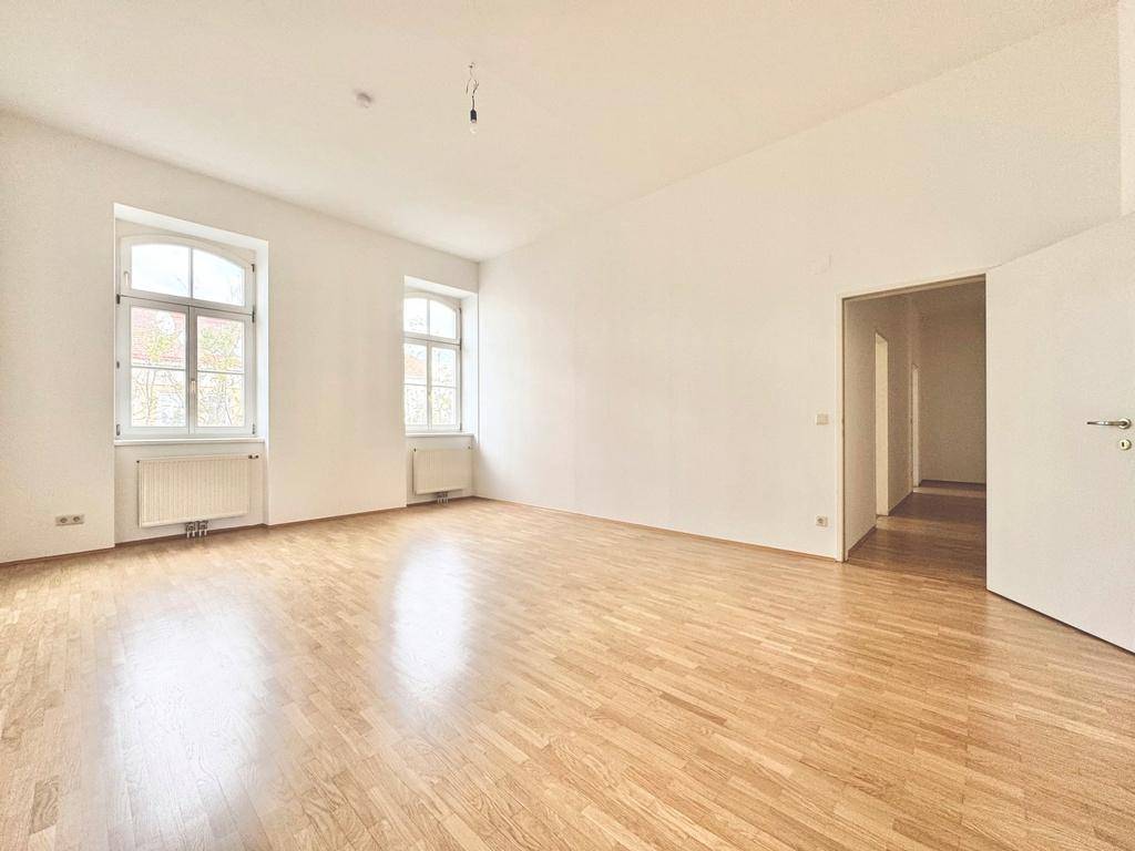 Lichtdurchfluteter Raum mit klassischem Parkettboden und hohen Decken, ideal für Wohn- oder Schlafbereich.