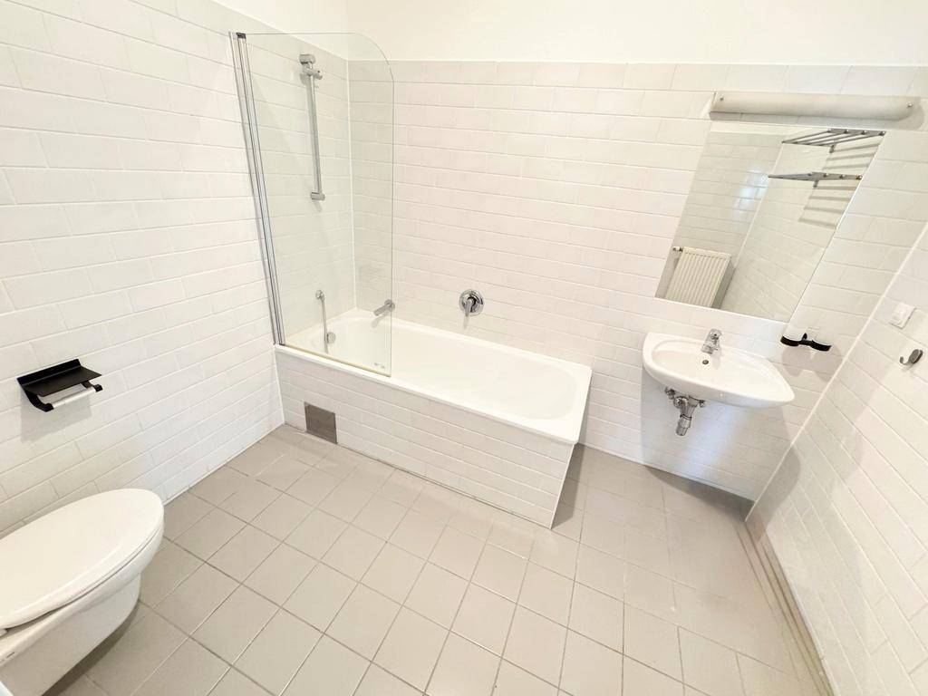 Modernes Badezimmer mit Badewanne, Dusche, WC und Waschbecken, komplett gefliest in Weiß und Grau.