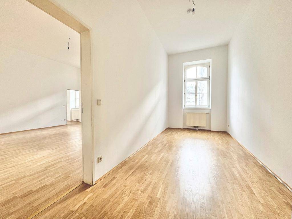 Lichtdurchflutetes Zimmer mit Parkettboden und einem Fenster, ideal als Schlaf- oder Arbeitszimmer.