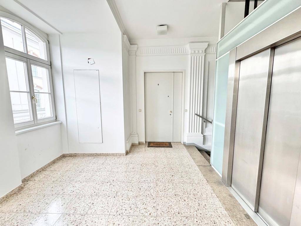 Heller Eingangsbereich mit Aufzug, großem Fenster und Terrazzoboden, der zum Wohnbereich führt.