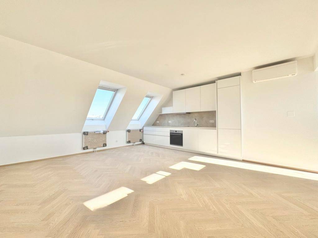 Offener Wohnbereich mit integrierter moderner Küche, Fischgrätparkett und schrägen Dachfenstern.