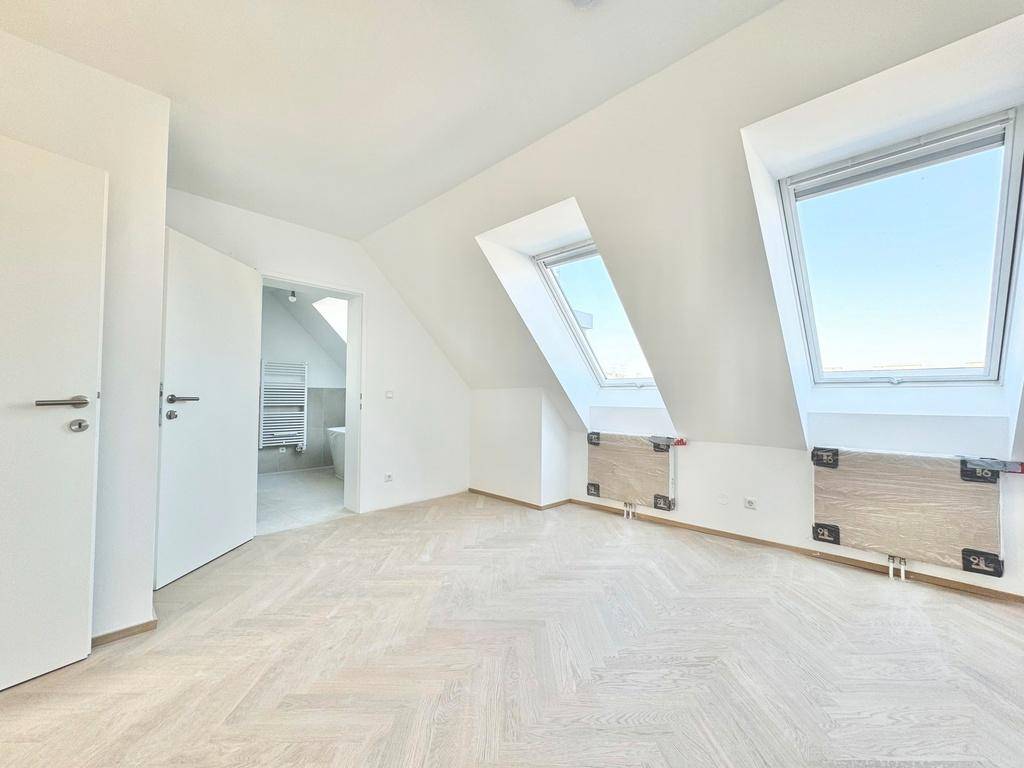 Helles Schlafzimmer im Dachgeschoss mit Fischgrätparkett, Dachfenstern und Zugang zu einem Badezimmer.