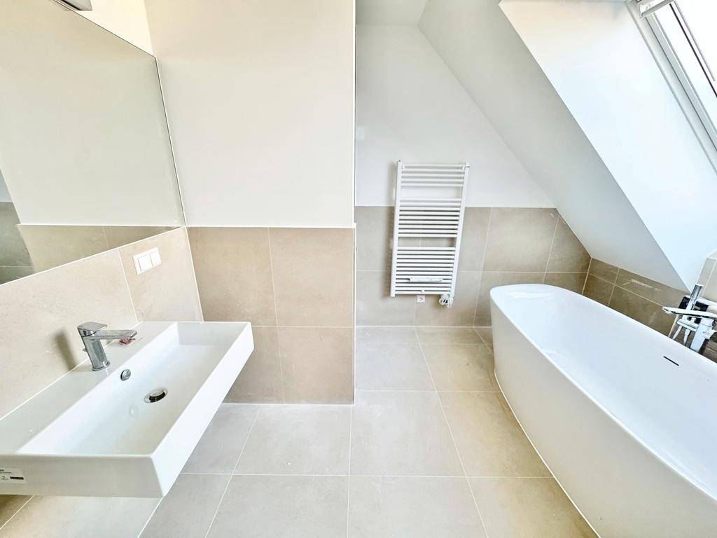 Modernes Badezimmer mit freistehender Badewanne, Waschtisch und beheiztem Handtuchhalter unter einem Dachfenster.