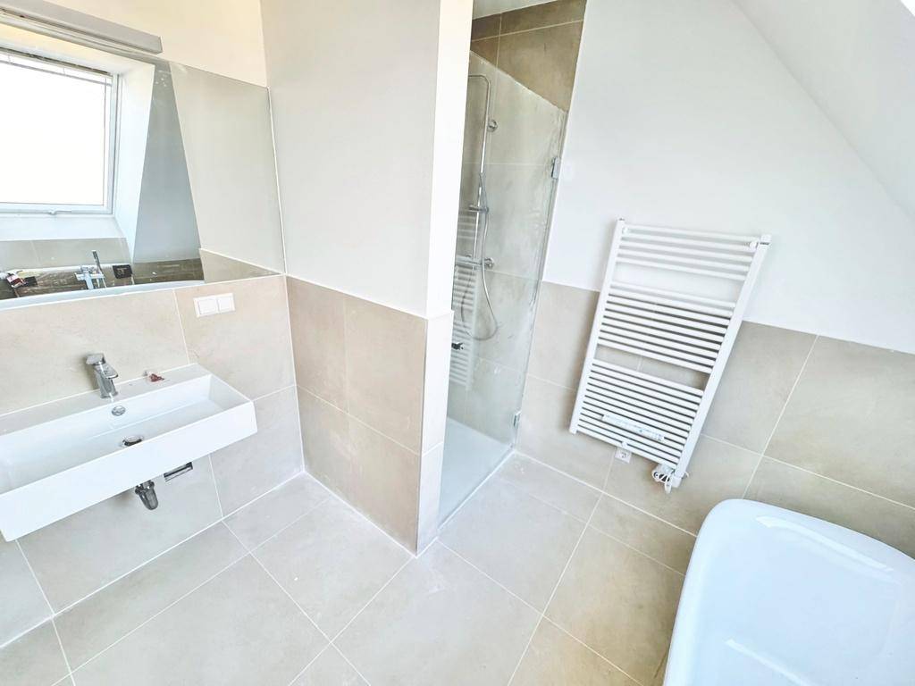 Helles Badezimmer mit begehbarer Dusche, Waschtisch, WC und beheiztem Handtuchhalter im Dachgeschoss.