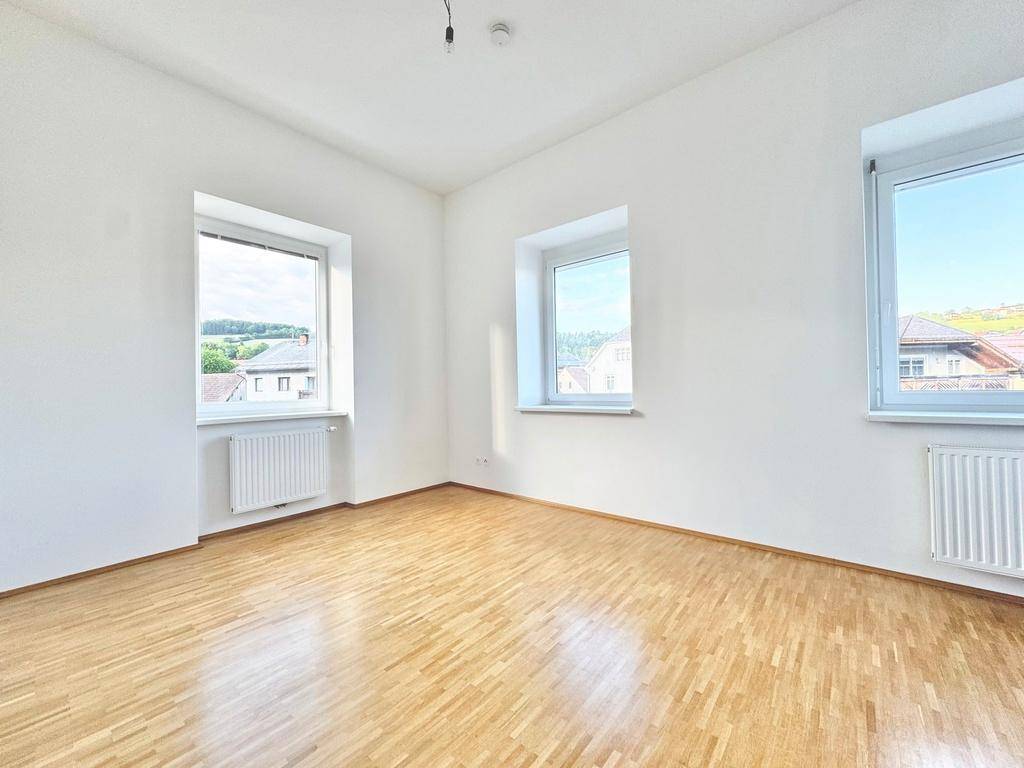 Helles Zimmer mit Parkettboden und mehreren Fenstern, geeignet als Schlaf- oder Arbeitszimmer.