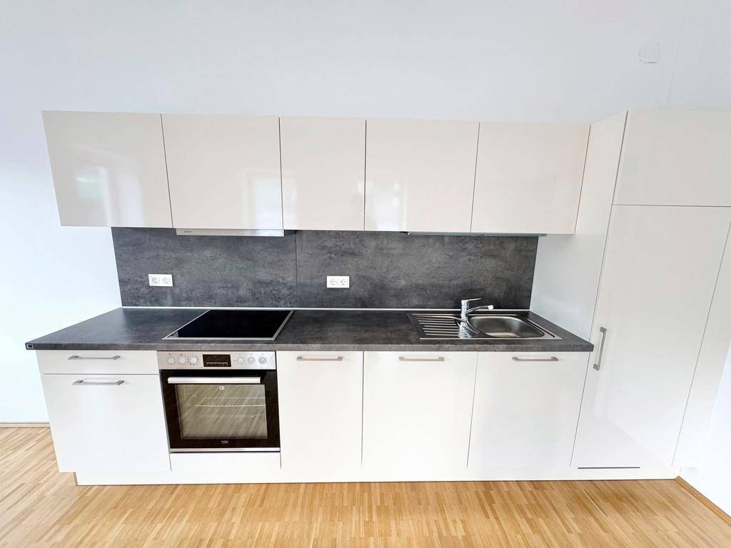 Moderne Einbauküche mit weißen Hochglanzfronten, dunkler Arbeitsplatte und integrierten Geräten.