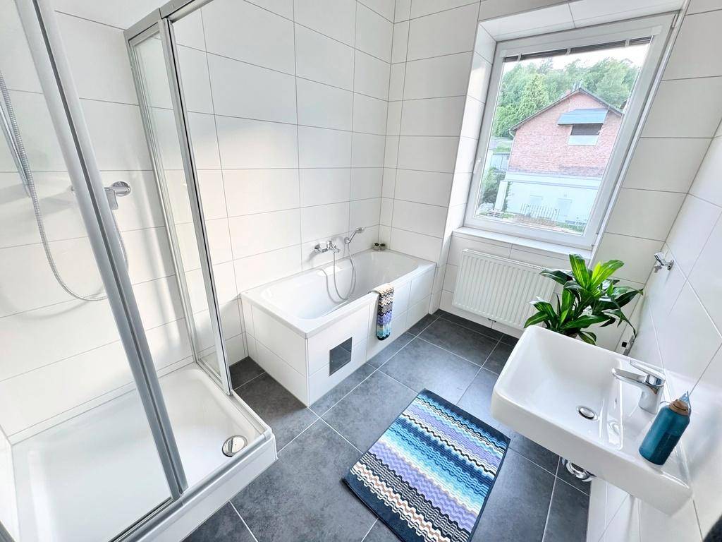Modernes Badezimmer mit weißen Fliesen, Dusche, Badewanne und Fenster für Tageslicht.