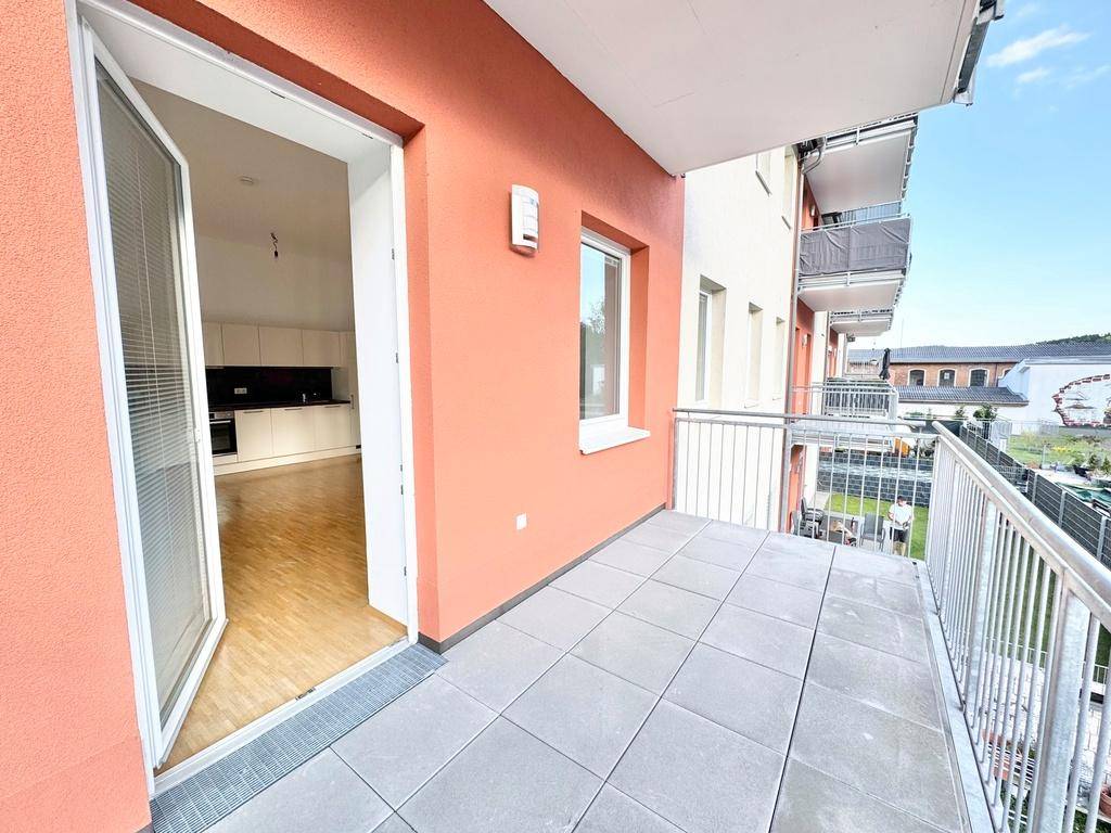 Balkon mit Fliesenboden und Zugang zu einem hellen Innenraum mit moderner Küche.