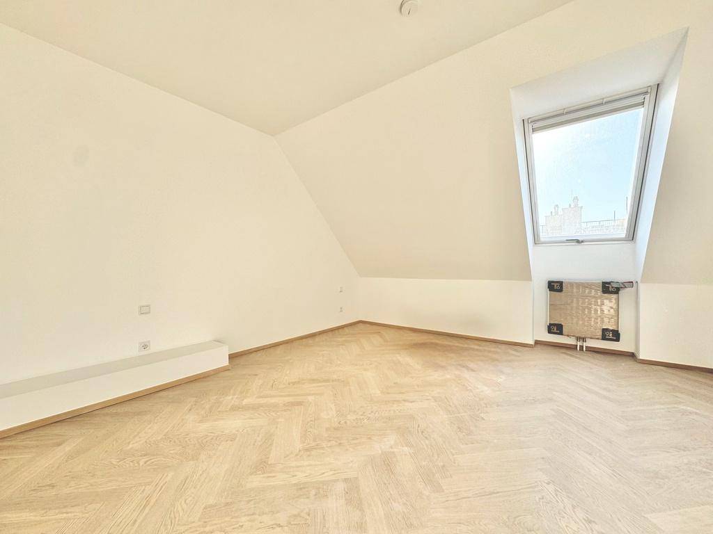 Geräumiges Dachzimmer mit hellem Fischgrätparkett und großem Dachfenster.